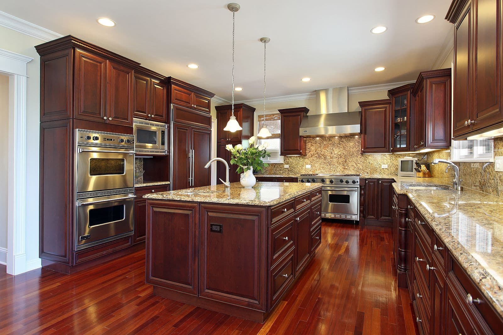 Luxury kitchen with dark cherry cabinets, granite countertops, stainless steel appliances, island with pendant lighting, and hardwood flooring